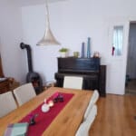 Jasny salon w mieszkaniu w Opolu z dużym drewnianym stół, pianinem i kozą grzewczą
